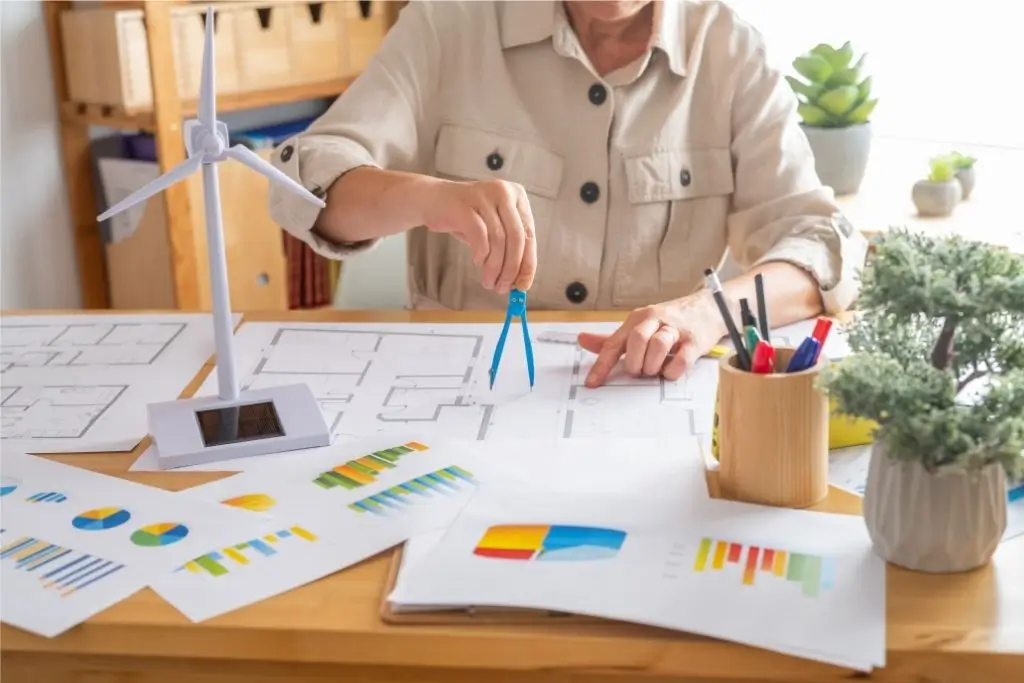 Eine Fachperson arbeitet an technischen Zeichnungen und Diagrammen, neben einem Modell einer Windturbine und verschiedenen Analyseunterlagen.