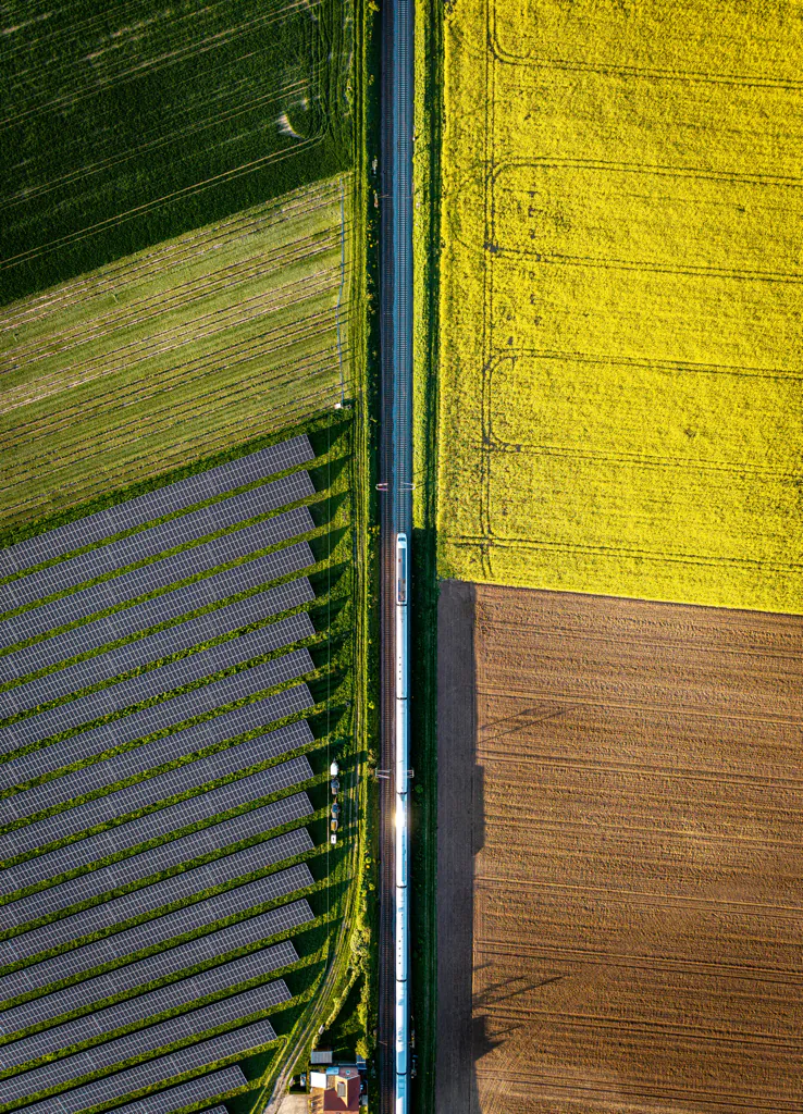 A bird's eye view of a ground-mounted photovoltaic system next to a rapeseed field and railroad line