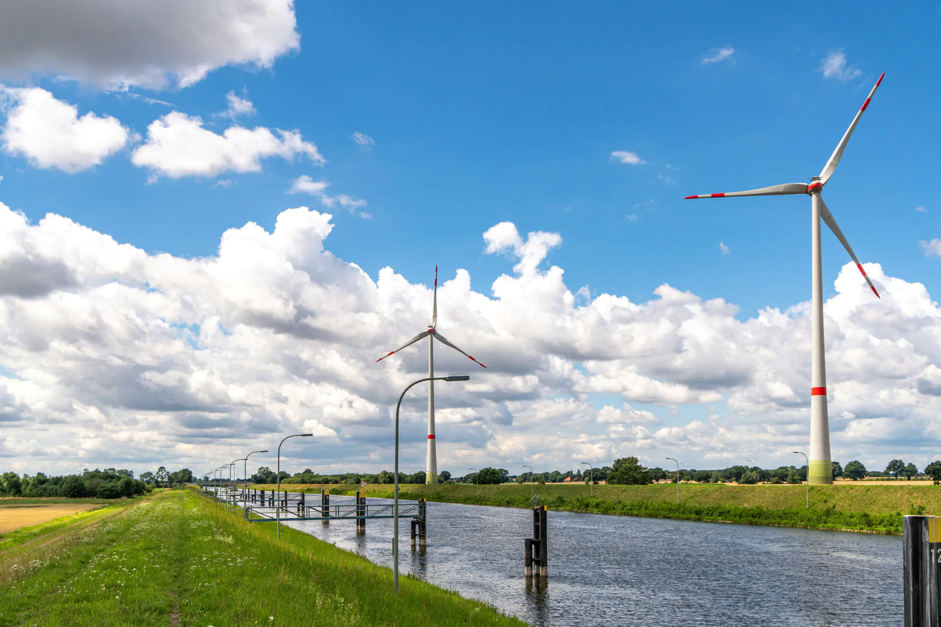 Wind turbines on a canal in a flat landscape in northern Germany under a cloudy sky