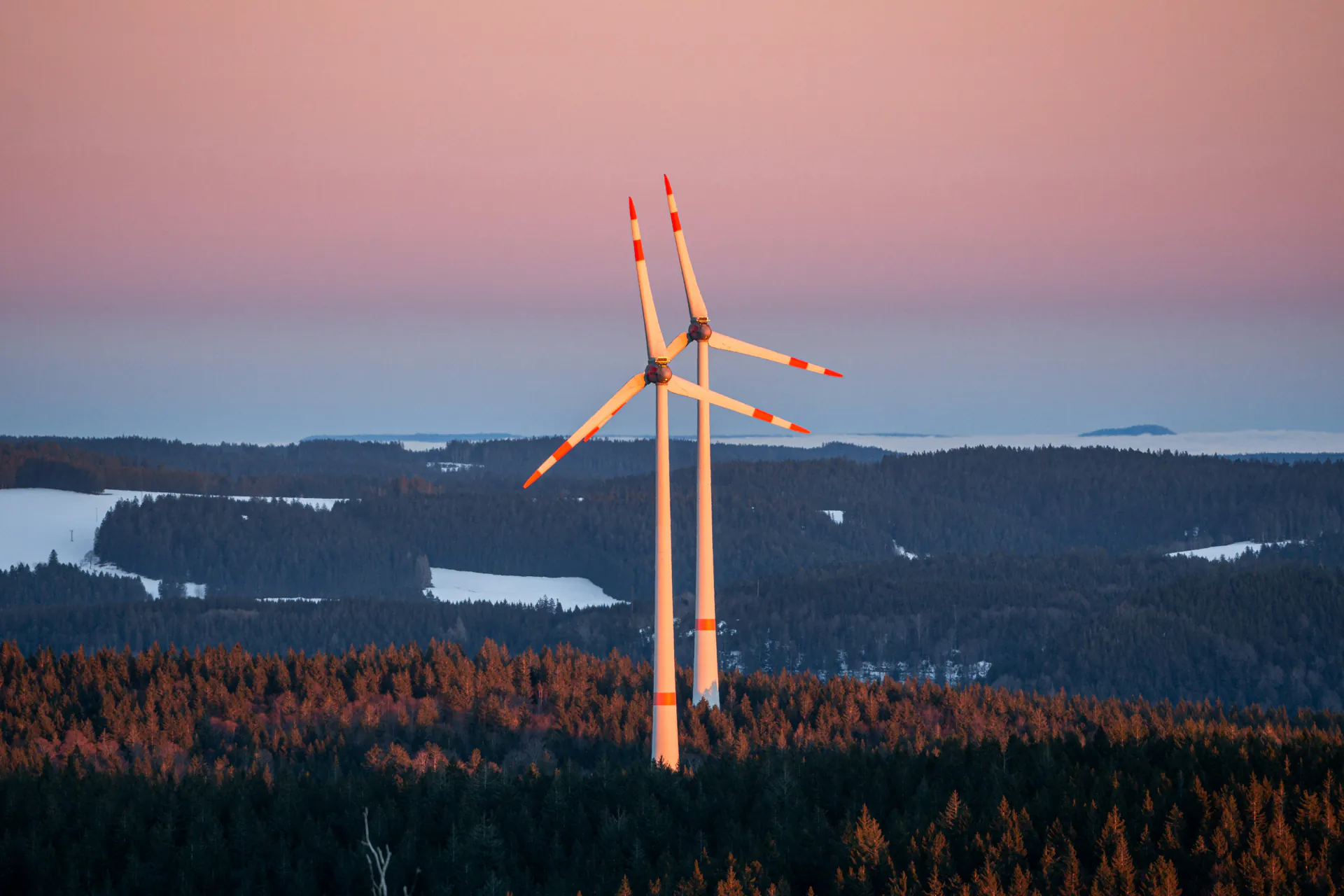 Veterné turbíny v zalesnenej krajine pri západe slnka